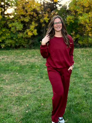 Model wearing a burgundy matching set with a crewneck long-sleeve top and wide-leg pants.