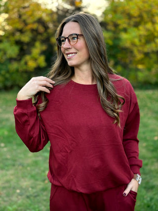 Front close-up of a burgundy crewneck top with long sleeves, dropped shoulders, and a relaxed fit.