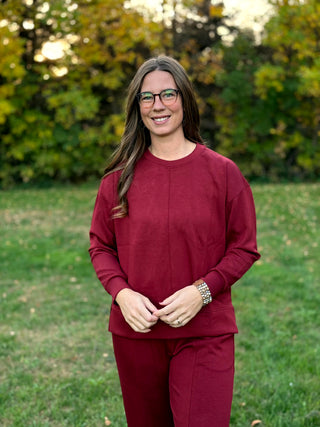 "Woman standing facing the camera in a burgundy crewneck sweatshirt and matching pants."