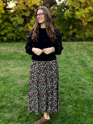 A lady wearing a polka dotted brown tone skirt.