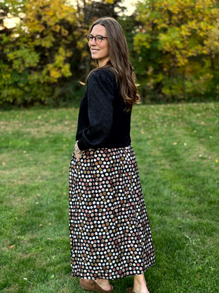 A lady wearing a polka dotted brown tone skirt.