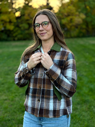 A lady wearing a brown plaid jacket with green corduroy collar and pockets.