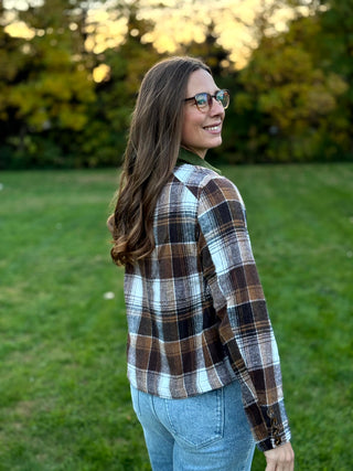 A lady wearing a brown plaid jacket with green corduroy collar and pockets.