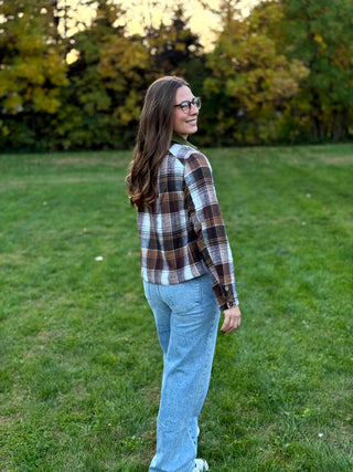 A lady wearing a brown plaid jacket with green corduroy collar and pockets.