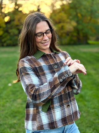 A lady wearing a brown plaid jacket with green corduroy collar and pockets.