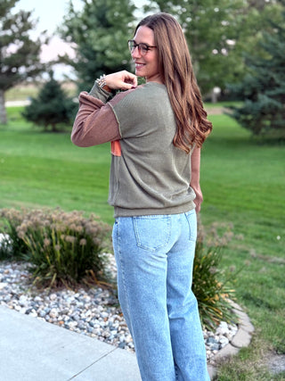 A lady wearing a brown, orange, and green colorblock textured top.