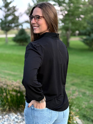 Close-up back view of a black blouse showing pleated shoulders, gathered cuffs, and a relaxed fit.