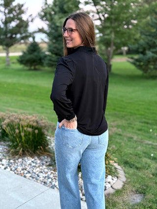 Back view of a black long-sleeve blouse with a stand collar and curved hem, styled with light-wash jeans.