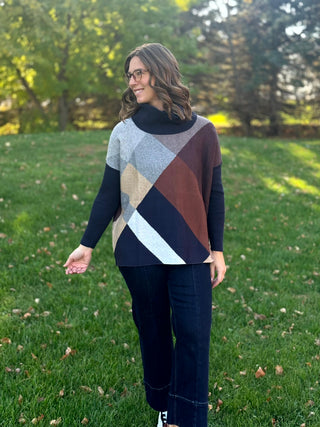 Full-length front view of the navy, gray, brown, and cream sweater paired with dark wide-leg jeans.