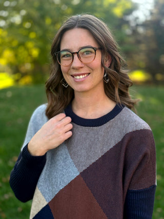 Close-up of a geometric colorblock sweater in navy, gray, brown, and cream with a ribbed crew neckline.