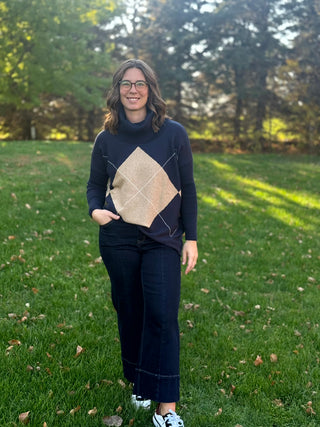 Full-length front view of the navy argyle cowl-neck sweater paired with dark cropped jeans and sneakers.
