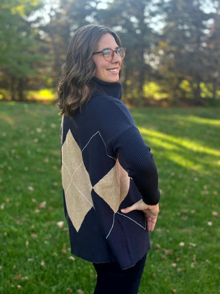 Close-up rear view showing the navy sweater’s beige diamond pattern, ribbed sleeves, and side-slit hem.