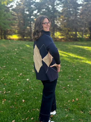 Full-length rear view of the navy sweater featuring beige argyle diamonds, styled with dark wide-leg jeans.
