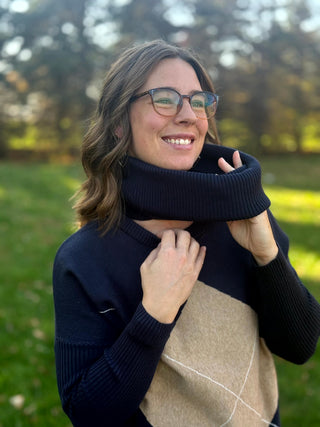 Close-up of the navy argyle sweater with the ribbed cowl neck held outward to show its width.