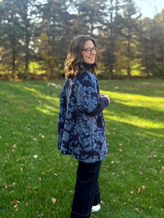 Side-back view of a model wearing a navy and slate-blue floral tunic with a loose fit and curved hem.
