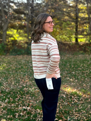 Side-back view of a cream knit sweater with muted pink and taupe stripes, ribbed hem, and long sleeves.