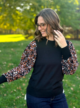 Angled front view of a black crewneck top with abstract-print balloon sleeves and wide black cuffs.