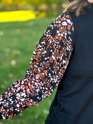 Close-up of the brown, pink, and white abstract-print balloon sleeve beside the textured black bodice.