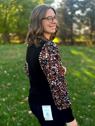 Three-quarter back view of a black top showing abstract-print sleeves and wide black cuffs.