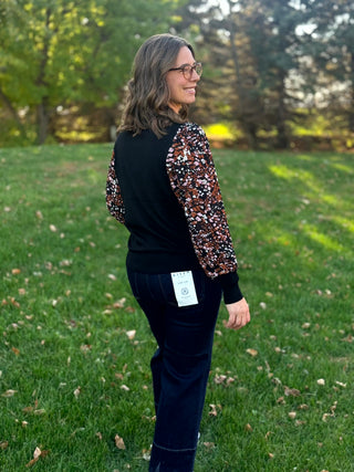 Back view of a black top with brown, pink, and white abstract-print balloon sleeves, styled with dark jeans.