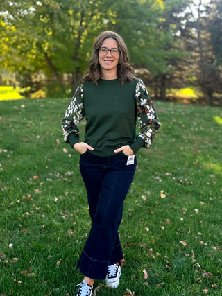 Full-length view of a model wearing a forest green leaf-sleeve top with dark wide-leg jeans and sneakers.⠋
