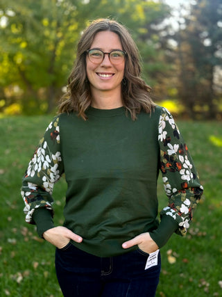 Front view of a forest green top with white, olive, and rust leaf-print sleeves and ribbed trim.