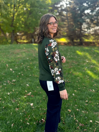 Side view of a model wearing a forest green top with relaxed leaf-print sleeves and ribbed cuffs.