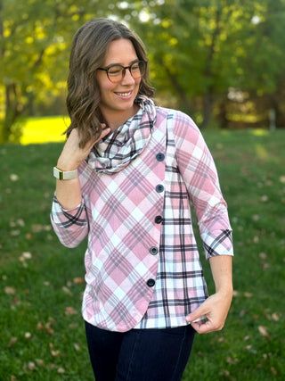 Front detail of the pink plaid top with a contrasting plaid cowl neck, asymmetrical button trim, and turned-back cuffs.
