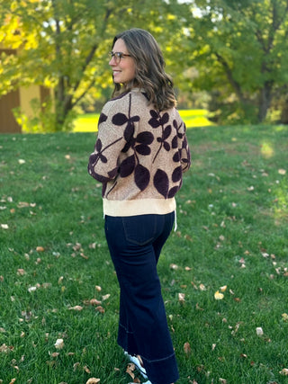 Full-length back view of a model wearing a taupe leaf-pattern sweater with dark wide-leg cuffed jeans.