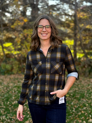 Model facing forward in a black, tan, and gray plaid button-up shirt with one sleeve rolled to show the light lining.