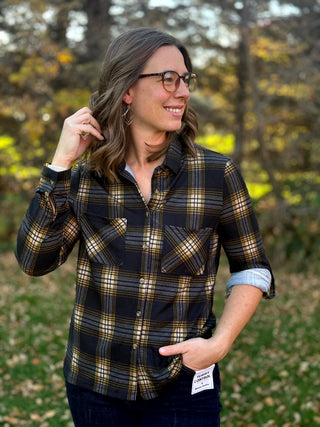 Close-up of a black, tan, and gray plaid shirt with a pointed collar, button front, and diagonal-plaid chest pockets.