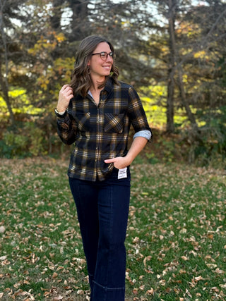 Front view of a model wearing a plaid button-up shirt with two chest pockets, a rolled sleeve, and dark jeans.