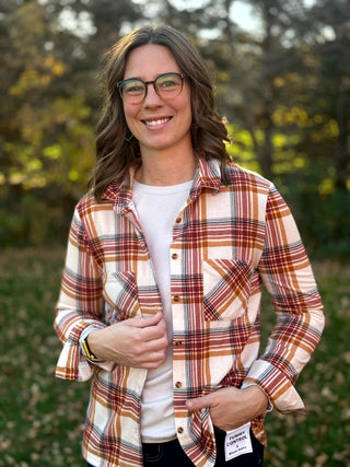 Front detail of a cream, rust, and tan plaid button-up shirt with two chest pockets, layered over a white tee.