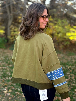 Back view of olive green sweatshirt with exposed seams and blue floral fabric bands on the sleeves.
