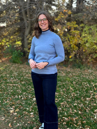 Model wearing a fitted light blue sweater with navy trim, styled with dark wide-leg jeans.