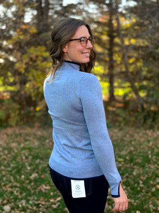 Back detail of a light blue sweater showing its ribbed hem, long sleeves, and navy-trimmed split cuffs.