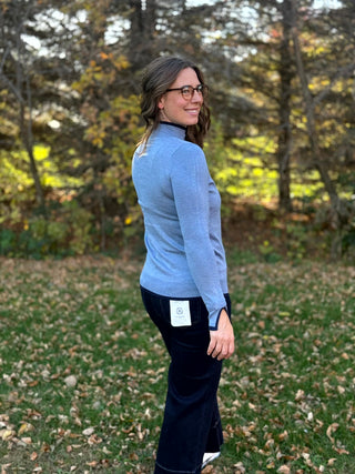 Three-quarter back view of a light blue mock-neck sweater paired with dark wide-leg jeans.