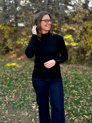 Black mock-neck sweater styled with dark-wash jeans, showing its fitted silhouette and hip-length hem.