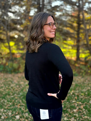 Back view of a black long-sleeve sweater with a ribbed hem, modeled with dark-wash jeans.