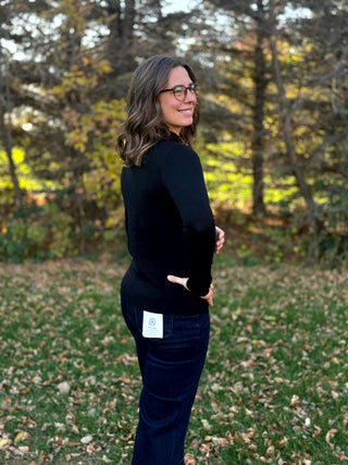 Side view of a fitted black mock-neck sweater, showing its hip-length cut.