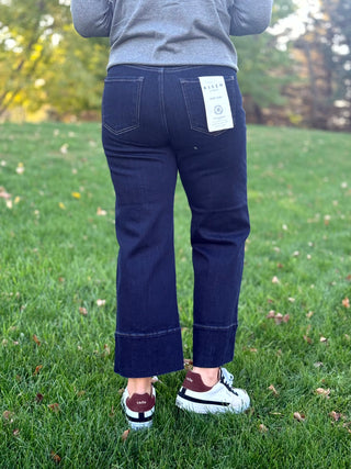 Back view of dark-wash cropped wide-leg jeans with two patch pockets and wide stitched hems.