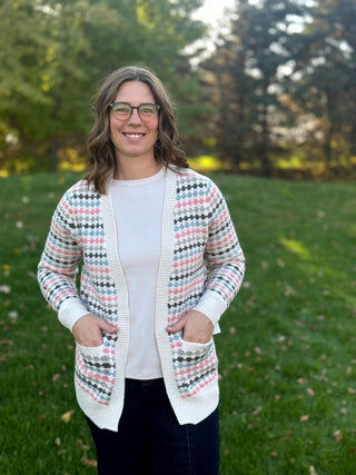 Close-up front view of the cream multicolor cardigan, showing ribbed edging and two patch pockets with the model’s hands tucked inside.