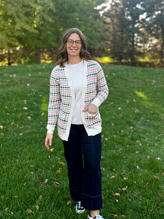 Full-length front view of a model wearing an open-front patterned cardigan with patch pockets, a white top, and dark wide-leg jeans.