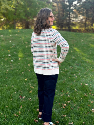 Three-quarter back view of a cream knit cardigan with pink, light blue, and charcoal patterned stripes and ribbed trim.