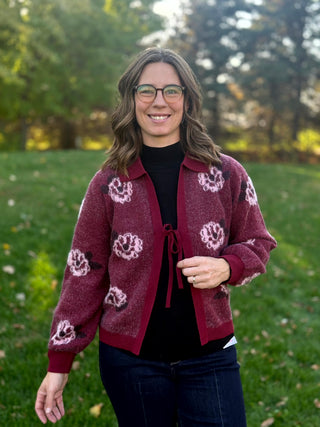 Model wearing a burgundy floral knit cardigan with a collar, tie-front closure, and ribbed cuffs and hem.