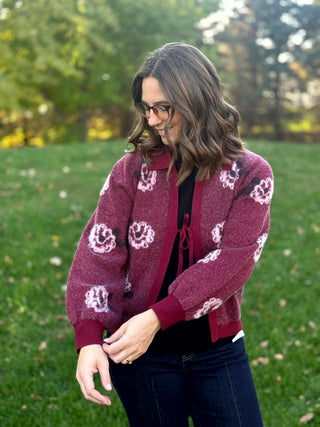 Close-up of a burgundy tie-front cardigan showing pale pink floral details and long sleeves with ribbed cuffs.
