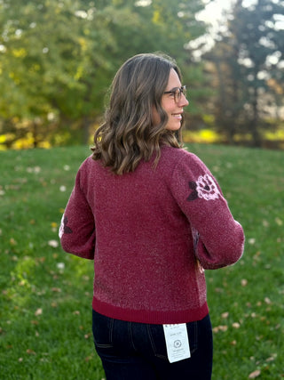 Back view of a burgundy knit cardigan showing a plain back, floral sleeves, and ribbed hem.