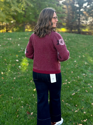 Full-length rear view of a model wearing a burgundy cardigan with dark wide-leg jeans and white sneakers.