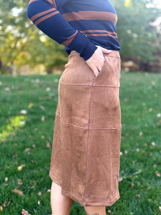 Side view of a camel-brown midi skirt showing an angled pocket and horizontal panel seams.