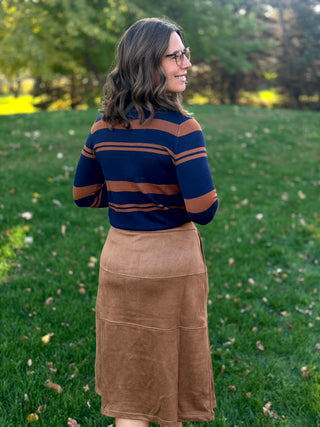Back view of a model wearing a camel-brown midi skirt with a navy and brown striped sweater.